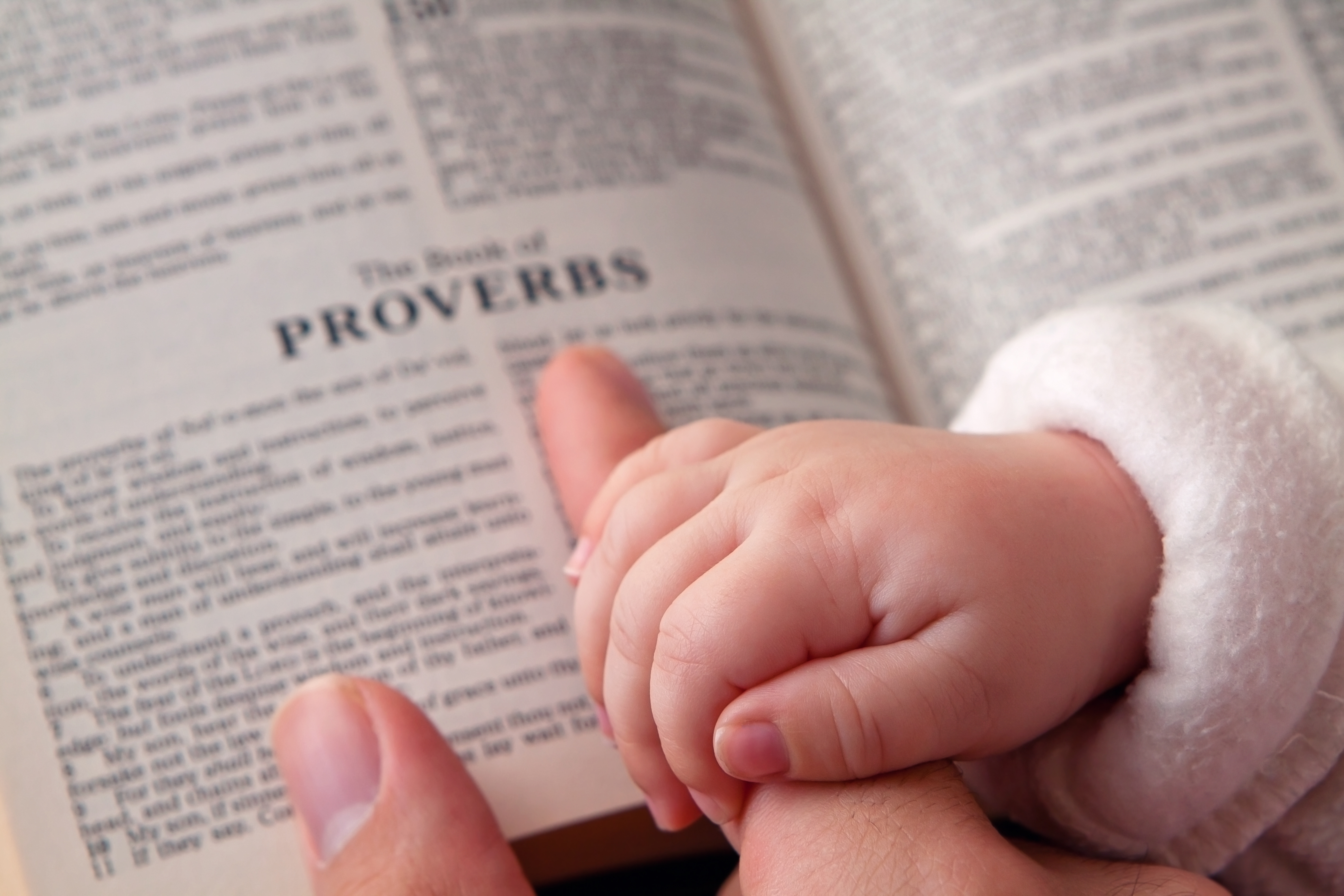 Baby holding father’s finger as he points to Proverbs verse