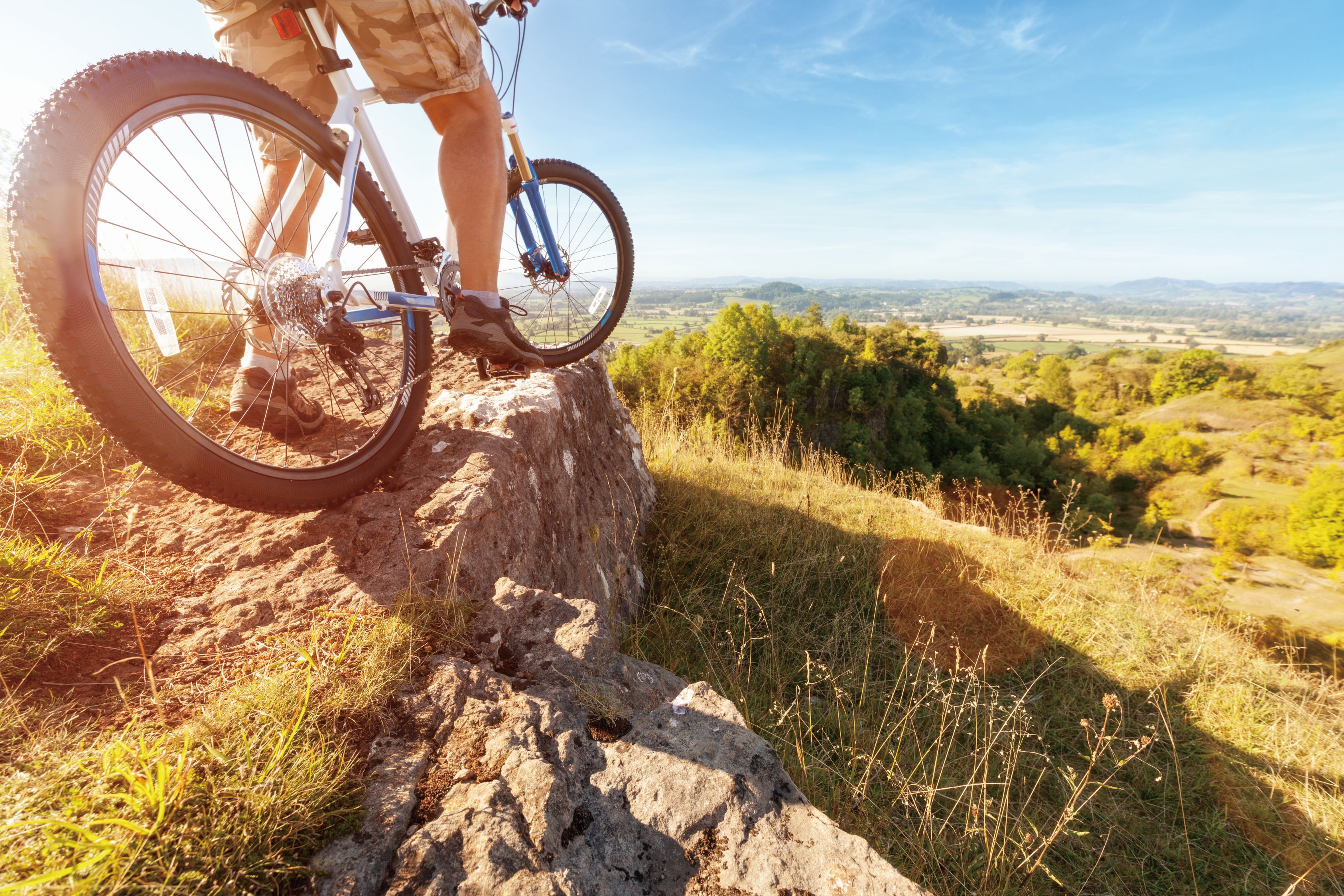 Mountain biker in action on rocks looking at downhill trail against blue sky concept for healthy lifestyle, excercise and extreme sports